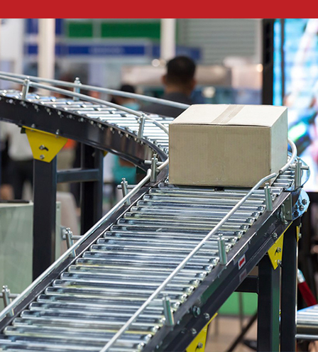 Full color image of a brown cardboard box moving down a conveyer in a busy warehouse